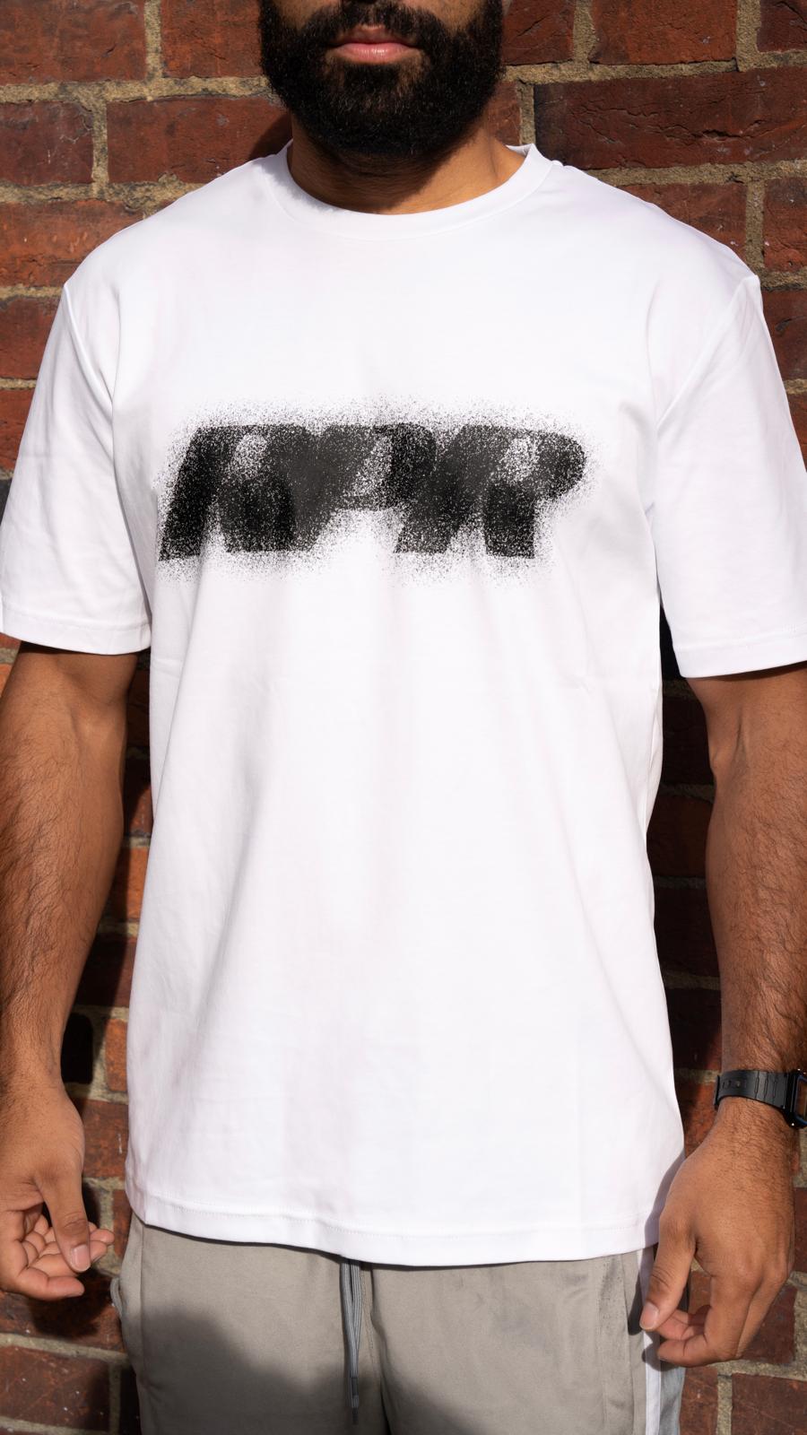 Model wearing white t-shirt with black spray logo graphic, standing against brick wall, styled with grey track pants